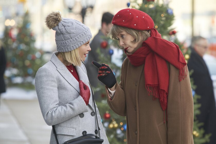 Still from A Shoe Addict's Christmas, depicting a woman (left) with short blonde hair, wearing a light gray coat, hat, and red gloves, looking over at a woman (right) with short dark blonde hair, wearing a brown coat, red scarf and beret, and black gloves.